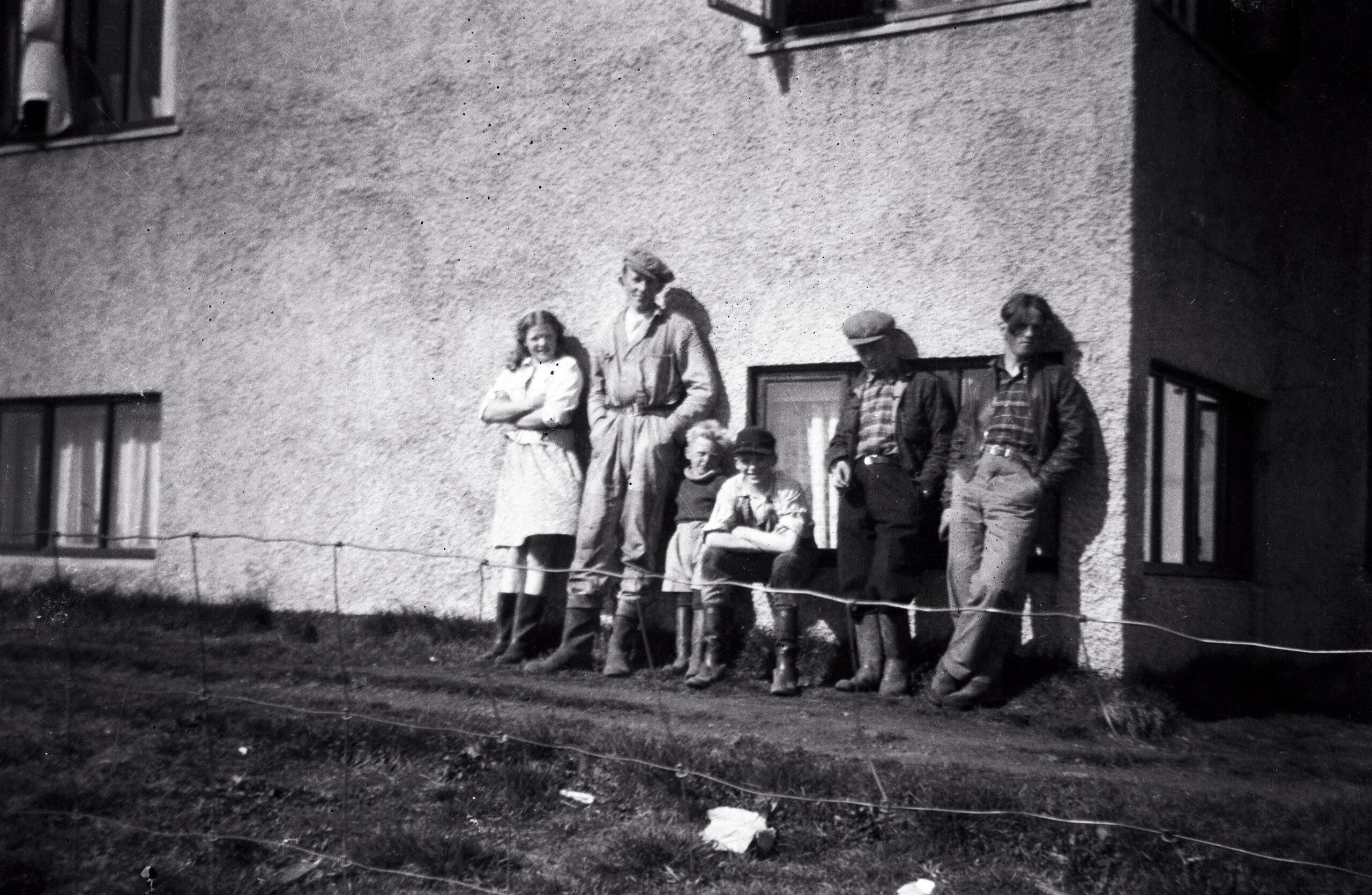 Farm workers and children by the farmhouse wall at Syðri-Reykir in Biskupstungur, between 1945 and 1955 — family archive photograph.
